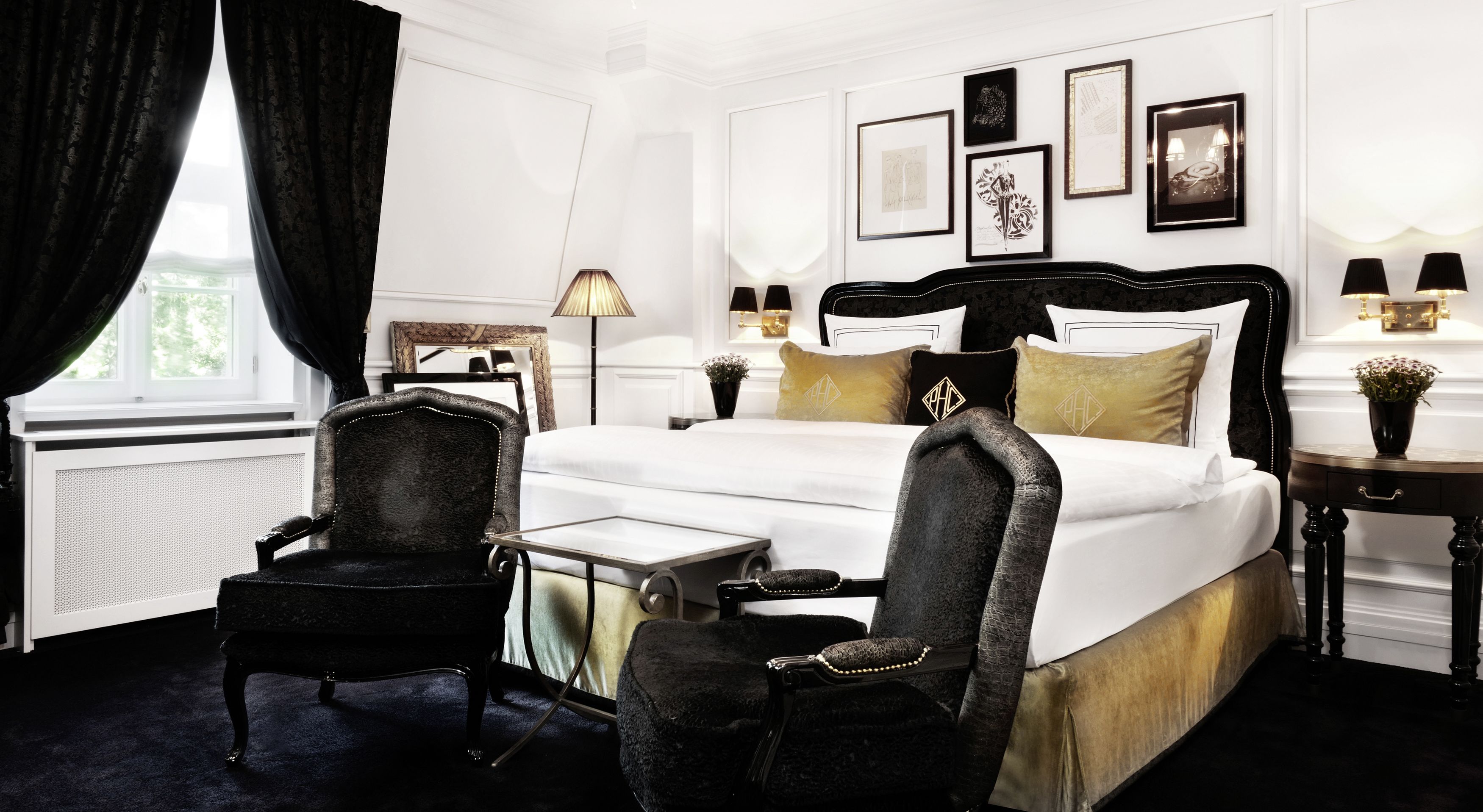 A hotel room with a large bed, two chairs, a small table, and a nightstand with lamps.