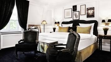 A hotel room with a large bed, two chairs, a small table, and a nightstand with lamps.