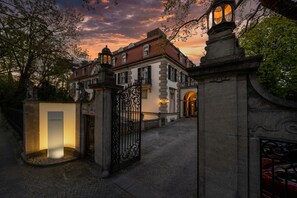 Un bâtiment historique doté d’une façade en pierre, d’une entrée protégée par un portail et d’un intérieur bien éclairé.