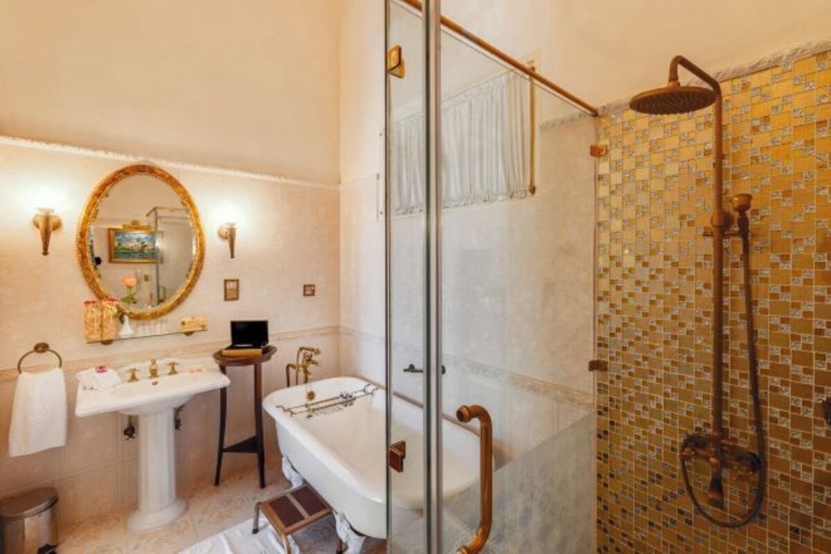 Un baño con bañera, ducha con mampara de vidrio y lavamanos con espejo.