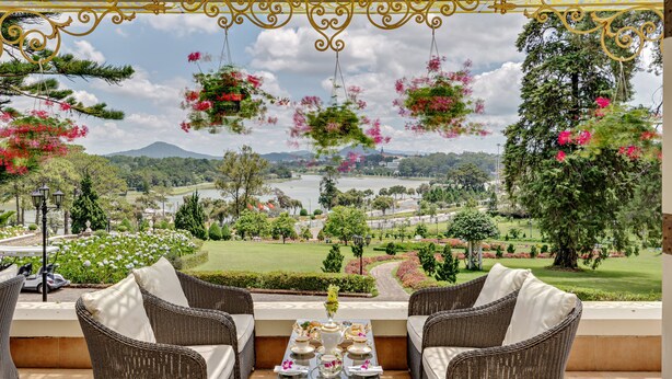 Una terraza con mobiliario de mimbre, una mesa con juego de té y macetas colgantes de flores.