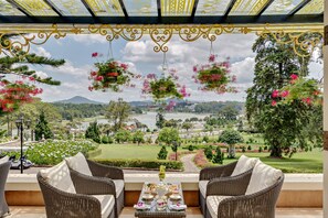 Una terraza con mobiliario de mimbre, una mesa con juego de té y macetas colgantes de flores.