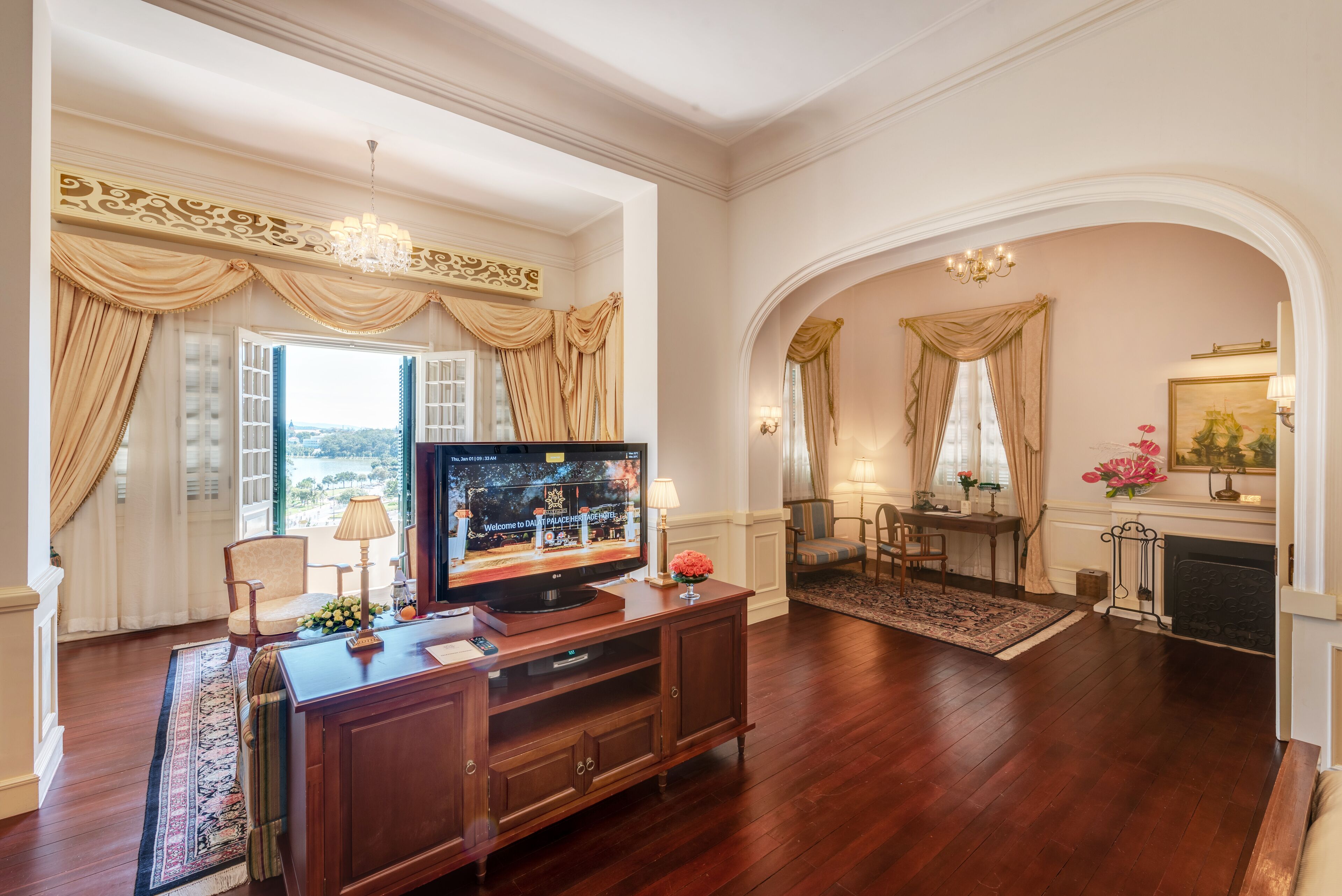 A spacious living room with a large flat-screen TV, wooden entertainment unit, and a fireplace.