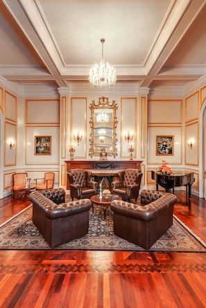 Una sala elegante con candelabro, sillones de cuero, un piano y chimenea.