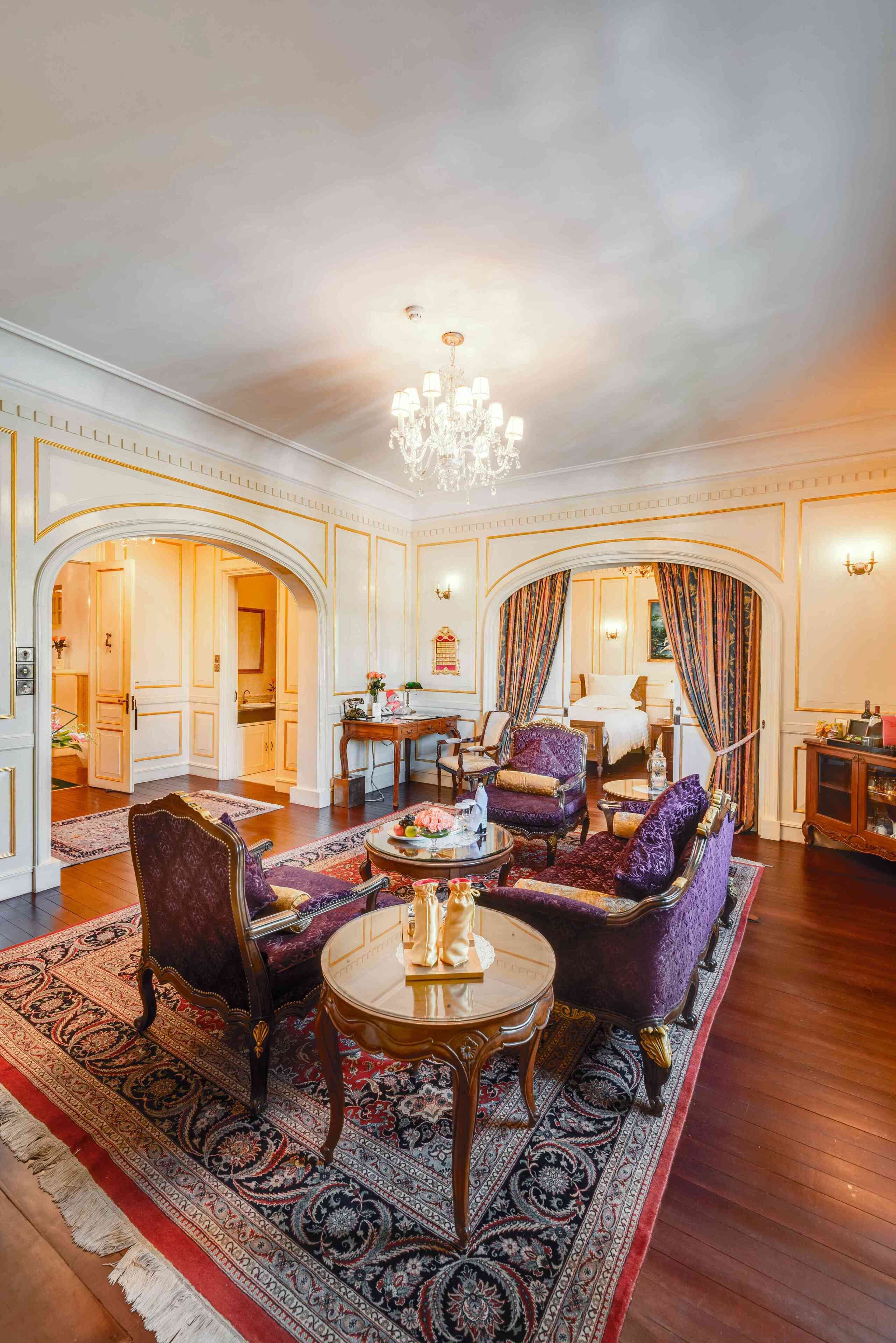 A luxurious living room with ornate furniture, a chandelier, and a large rug.