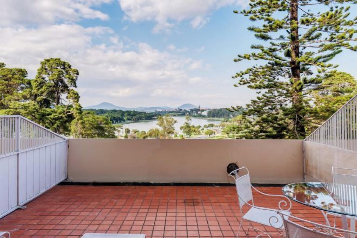 Un balcón con vistas a un lago, árboles y montañas a lo lejos.