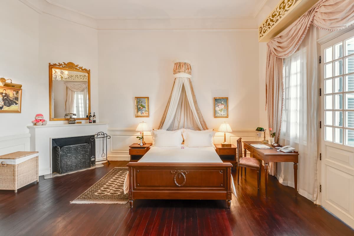 Een klassieke slaapkamer met een hemelbed, een open haard en een groot raam met gordijnen.