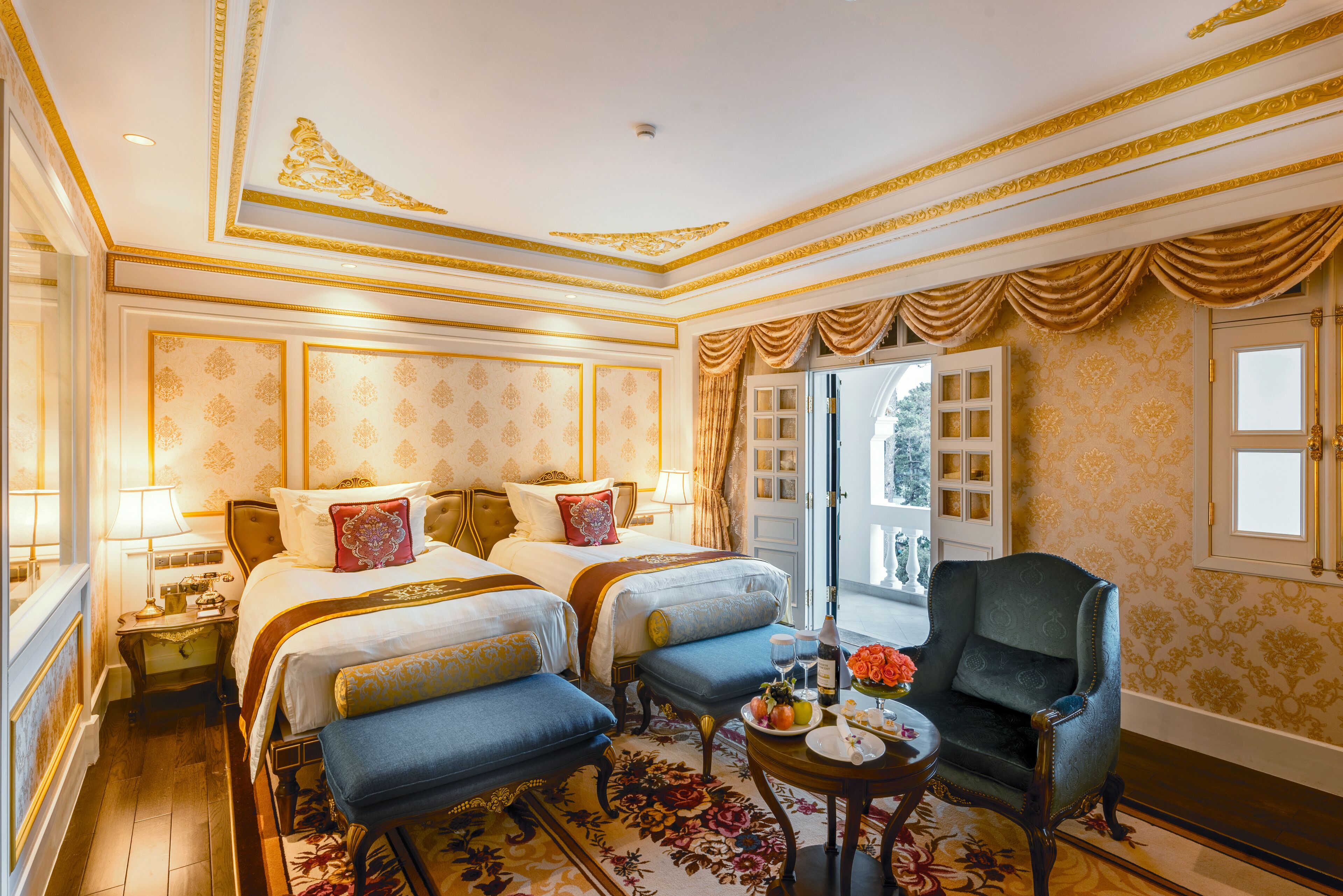 A luxurious hotel room with two beds, a sitting area, and a view of the outdoors.