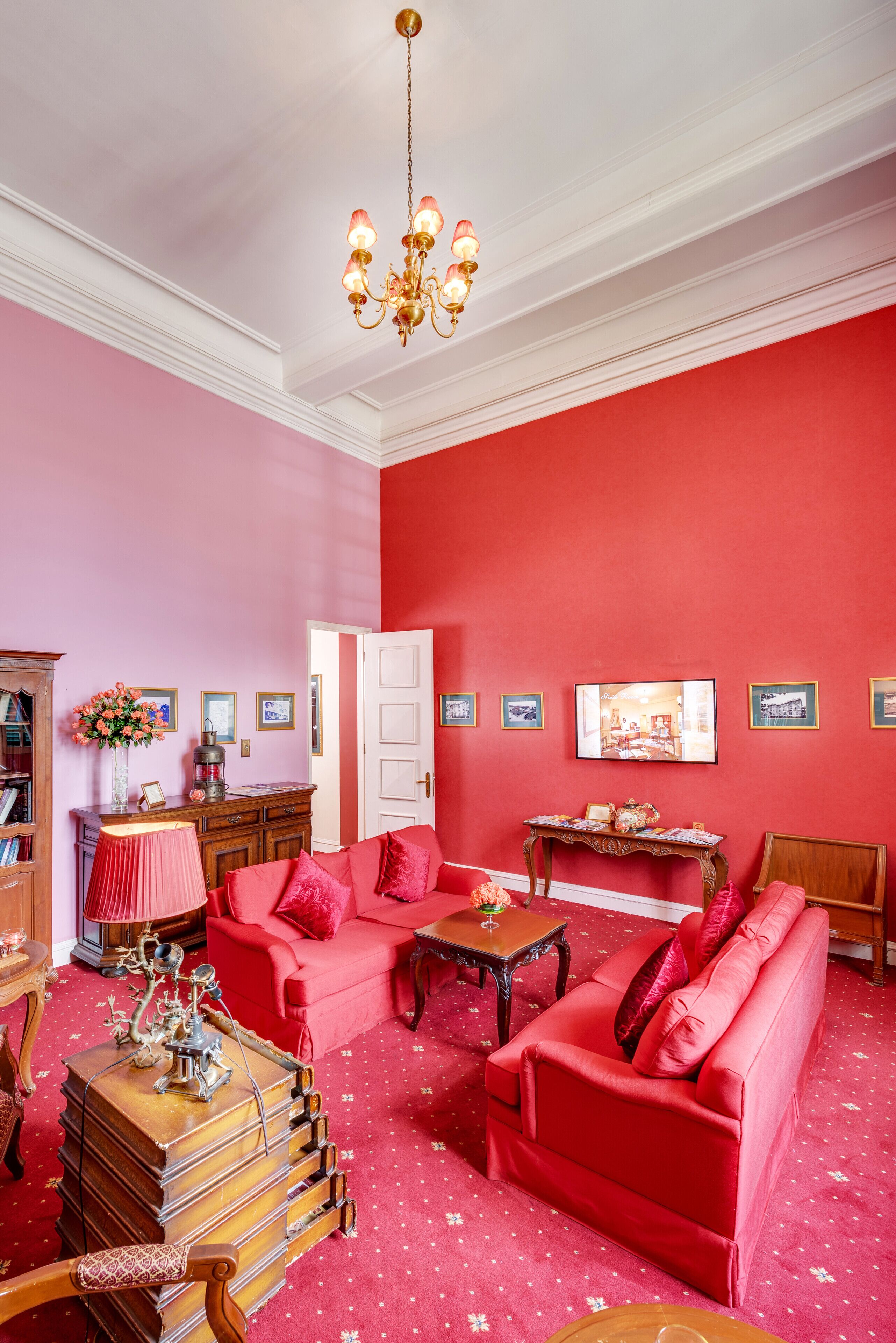A room with a red carpet, a red sofa, a wooden side table, a chandelier, and a bookshelf.