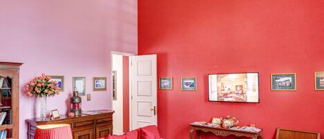 A room with a red carpet, a red sofa, a wooden side table, a chandelier, and a bookshelf.
