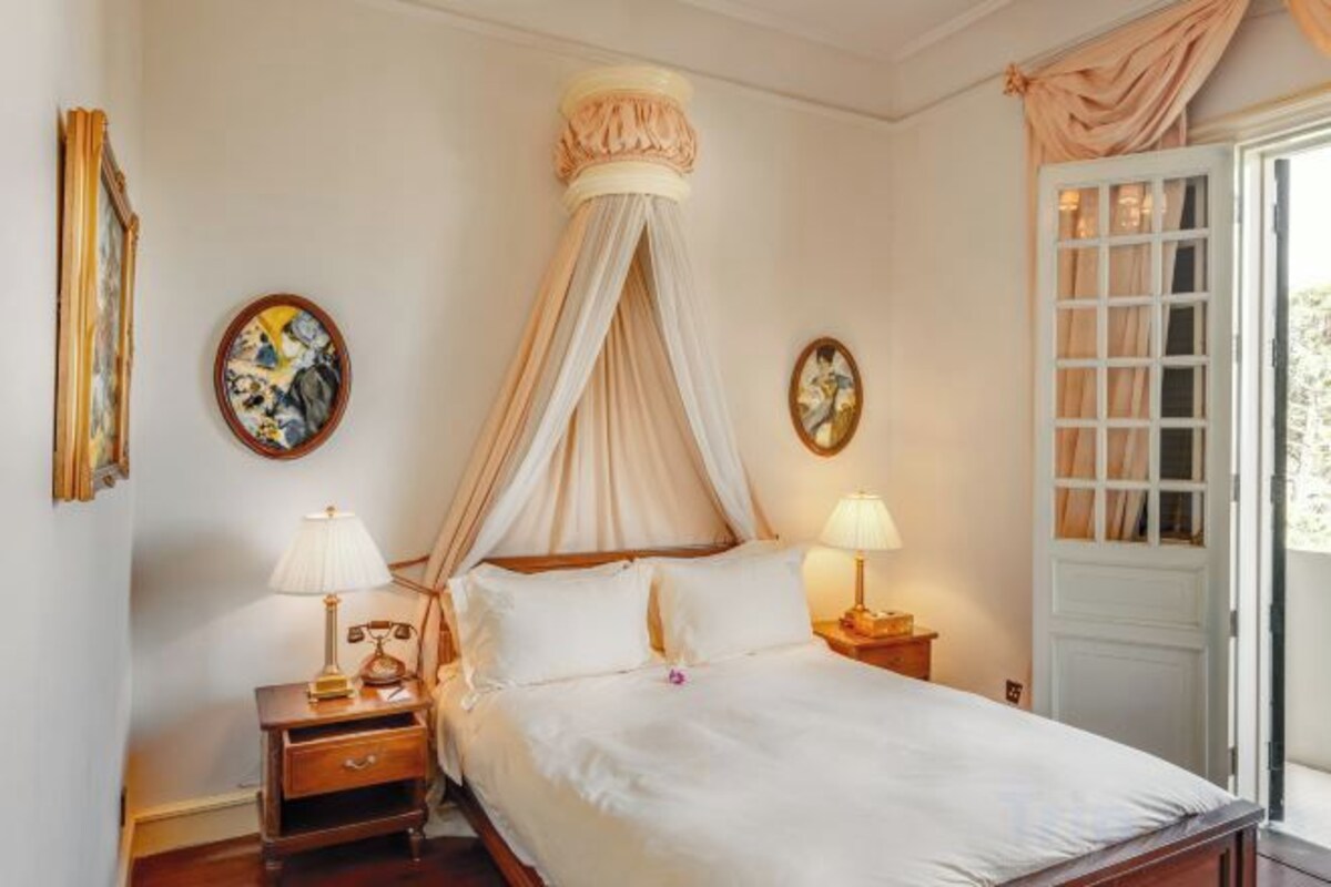 Un dormitorio con cama a dosel, mesitas de noche con lámparas y una puerta con vistas.