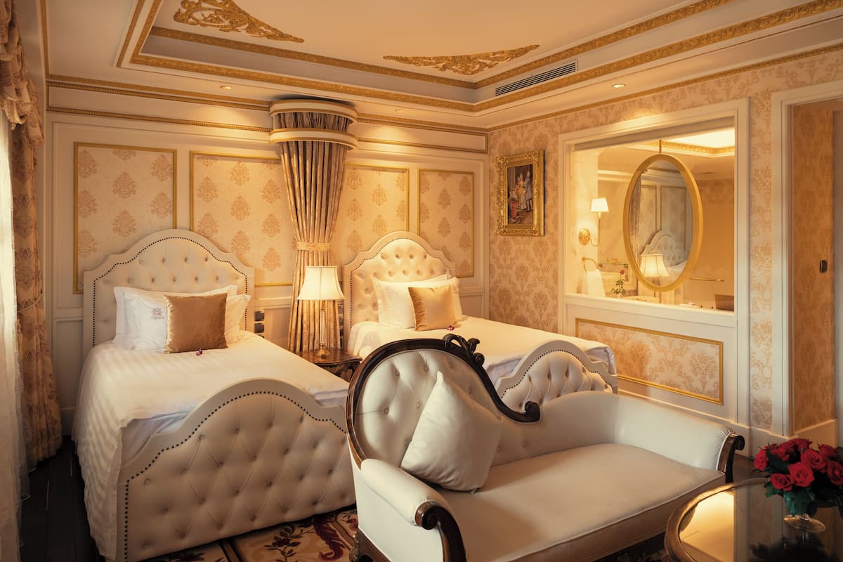 Een luxueuze slaapkamer met twee bedden, een bank, een spiegel en een kroonluchter.