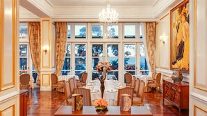 Comedor formal con una mesa de madera dispuesta para seis personas, sillas, una araña y ventanas grandes con cortinas.