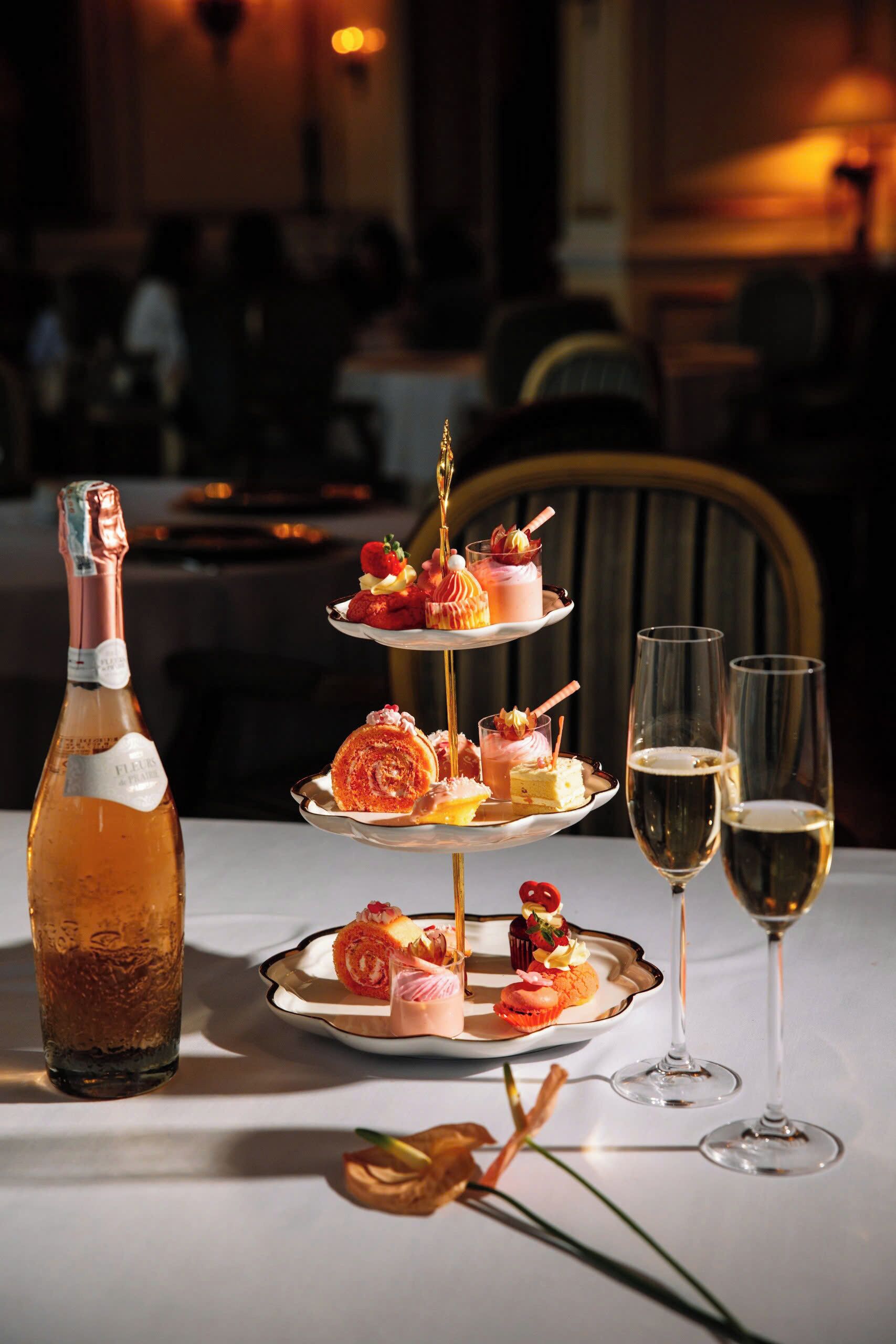 A three-tiered dessert stand with various pastries and a bottle of champagne on a table.