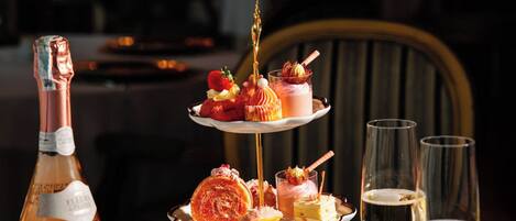 A three-tiered dessert stand with various pastries and a bottle of champagne on a table.