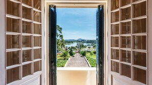 Vista a través de una puerta con múltiples ventanales que da a un sendero y un paisaje pintoresco con vegetación y una masa de agua.