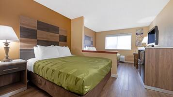 Habitació d'hotel amb llit, taula de nit, làmpada i zona de cuina equipada.