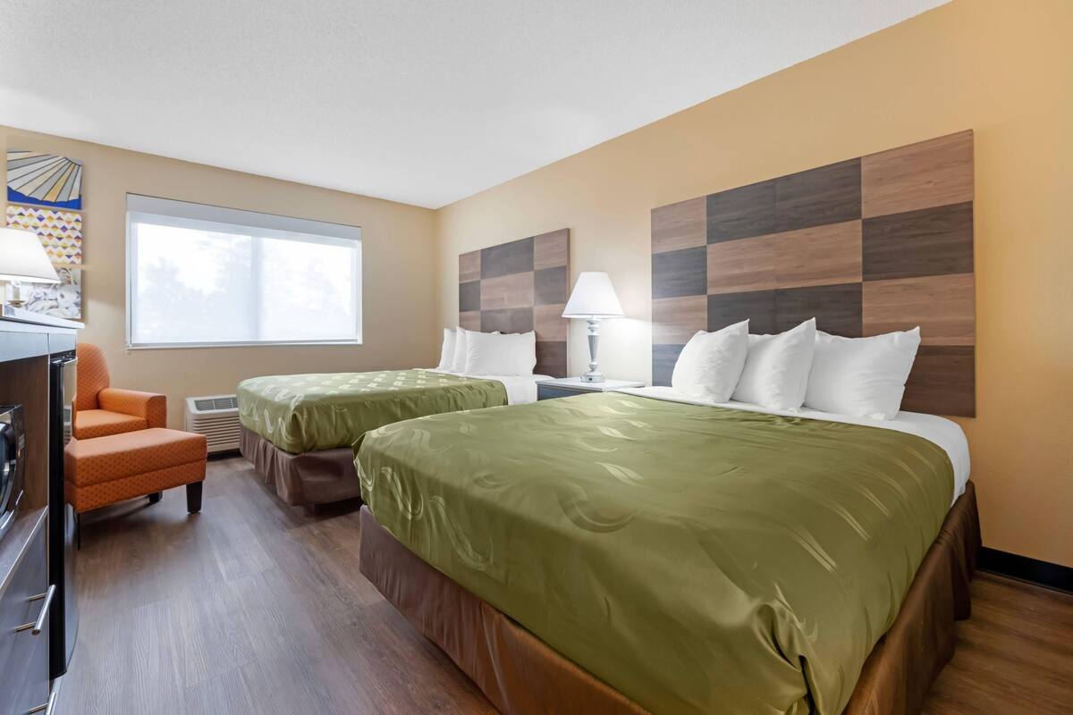 A hotel room with two beds, a desk, a chair, and a window.