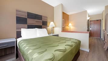 A hotel room with a bed, bedside table, lamp, and a mirror.