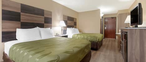 A hotel room with two beds, a desk with a TV, and a kitchenette.