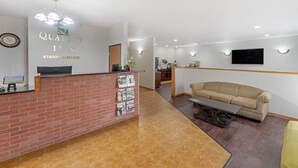 Un área de recepción con mostrador de ladrillo, un mostrador de recepción, un sofá, un televisor y un reloj montado en la pared.