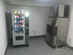 A vending machine and a refrigerator in a room with tiled flooring and a plain wall.