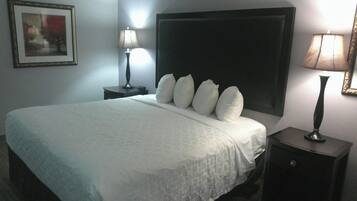 Un cuarto de hotel con una cama grande, dos mesitas de noche, una mesita auxiliar, un cuadro enmarcado en la pared y una lámpara en cada mesita de noche.