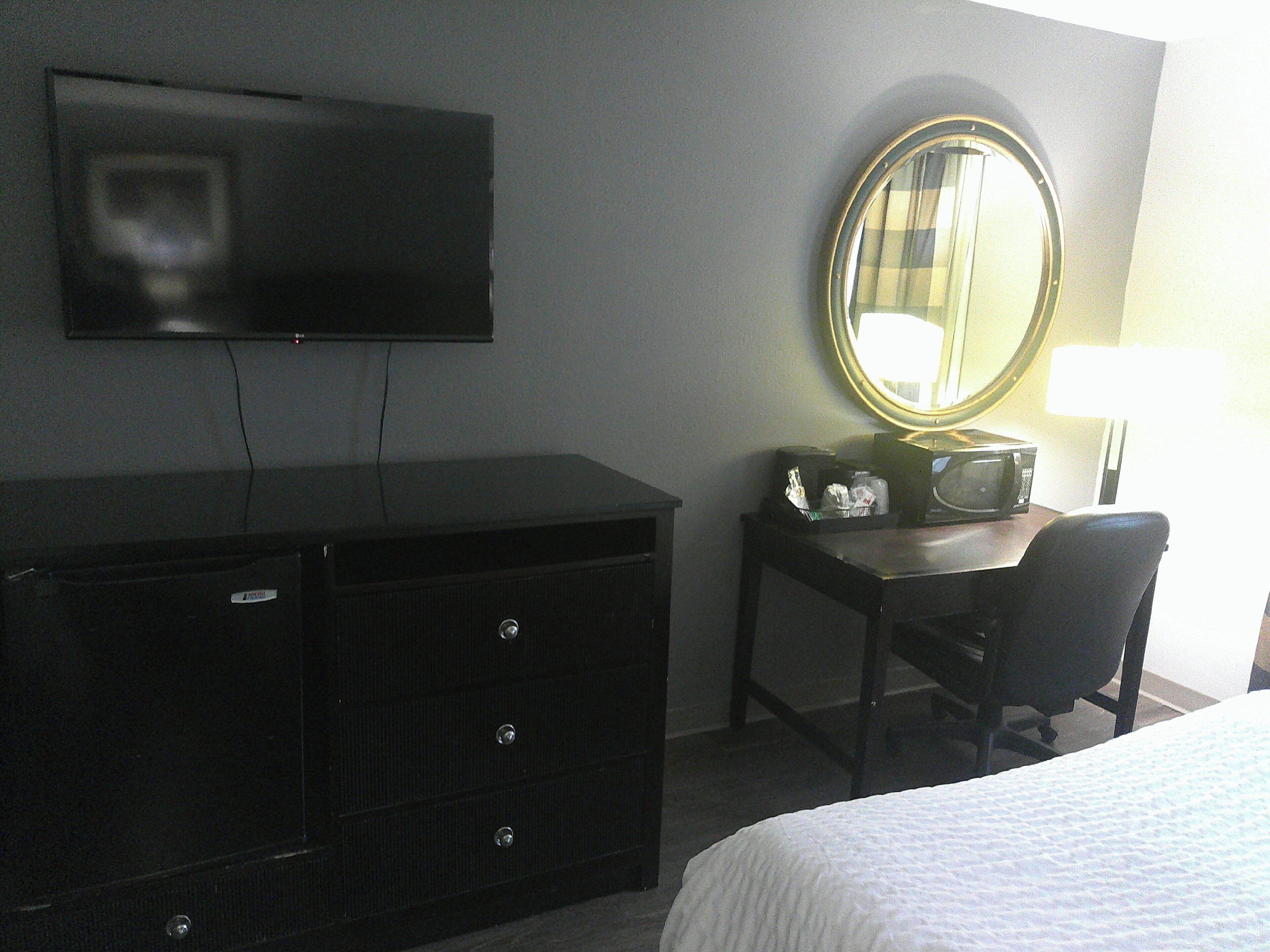 A hotel room with a TV, a desk with a mirror, a chair, and a bed.