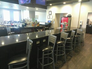 A bar area with a long counter, multiple stools, and a refrigerator with a Coca-Cola logo.
