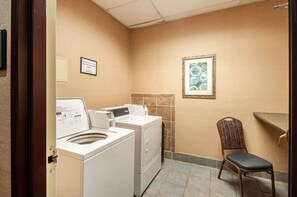 A laundry room with a washing machine, dryer, and a chair. - Carradoc Hall Hotel & Conference Center by The Red Collection (Leesburg)