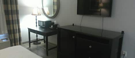 A hotel room with a bed, a dresser, a television mounted on the wall, and a lamp on the dresser.