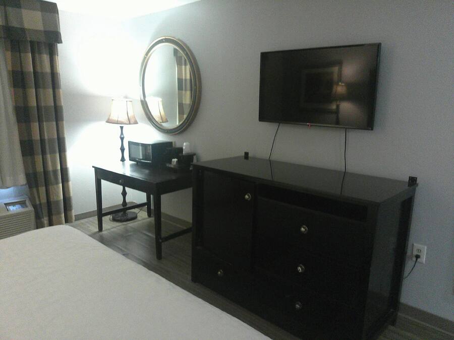Habitación de hotel con cama, cómoda, televisor montado en la pared y lámpara sobre la cómoda.