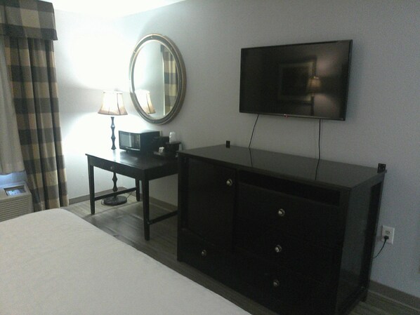 A hotel room with a bed, a dresser, a television mounted on the wall, and a lamp on the dresser.