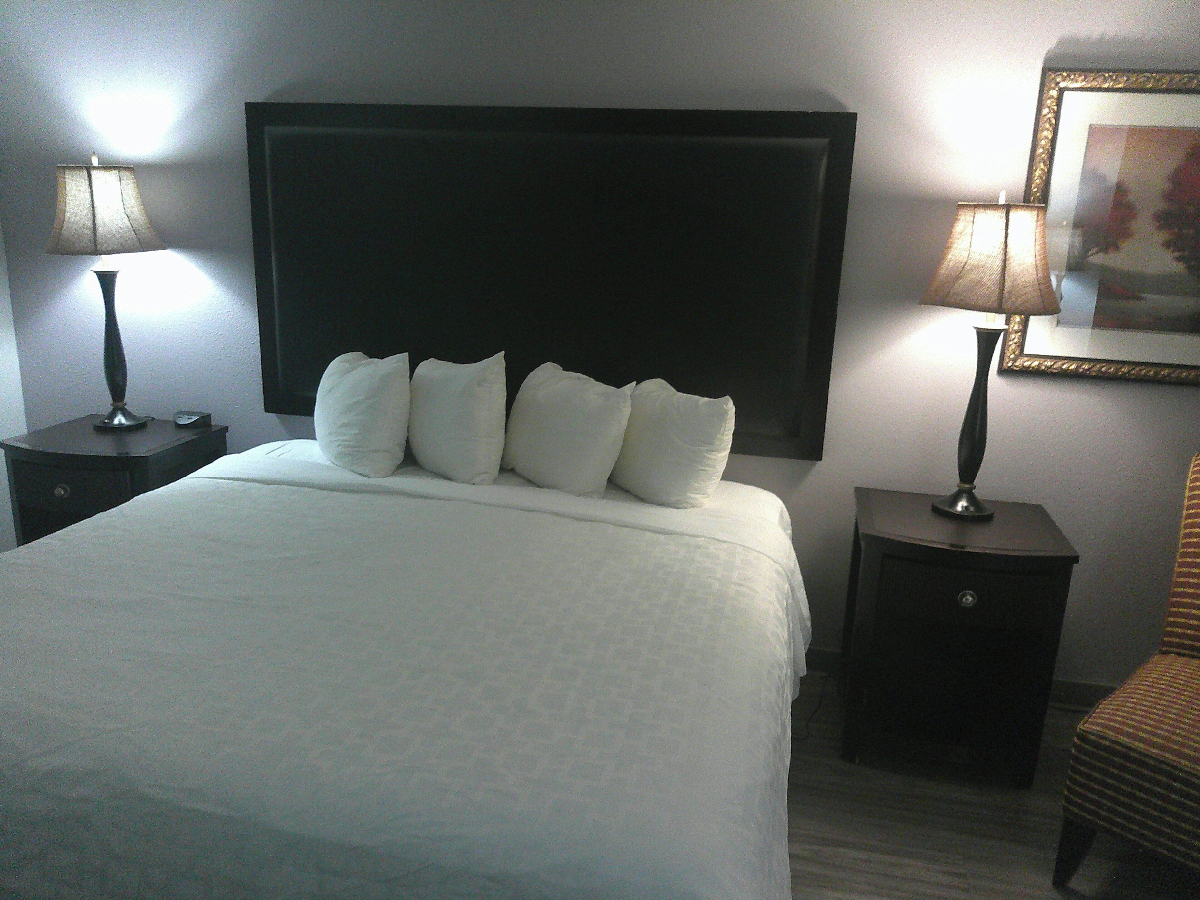 Una habitación de hotel con una cama grande, dos mesitas de noche y una silla.