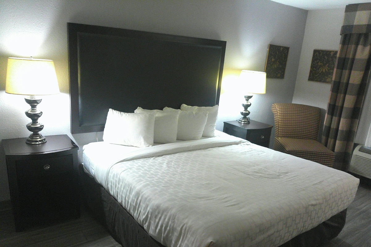 A hotel room with a large bed, two bedside tables with lamps, a chair, and a headboard.
