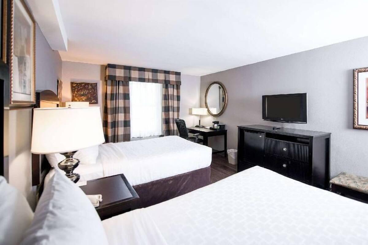 A hotel room with two beds, a desk, a chair, a TV, and a mirror.