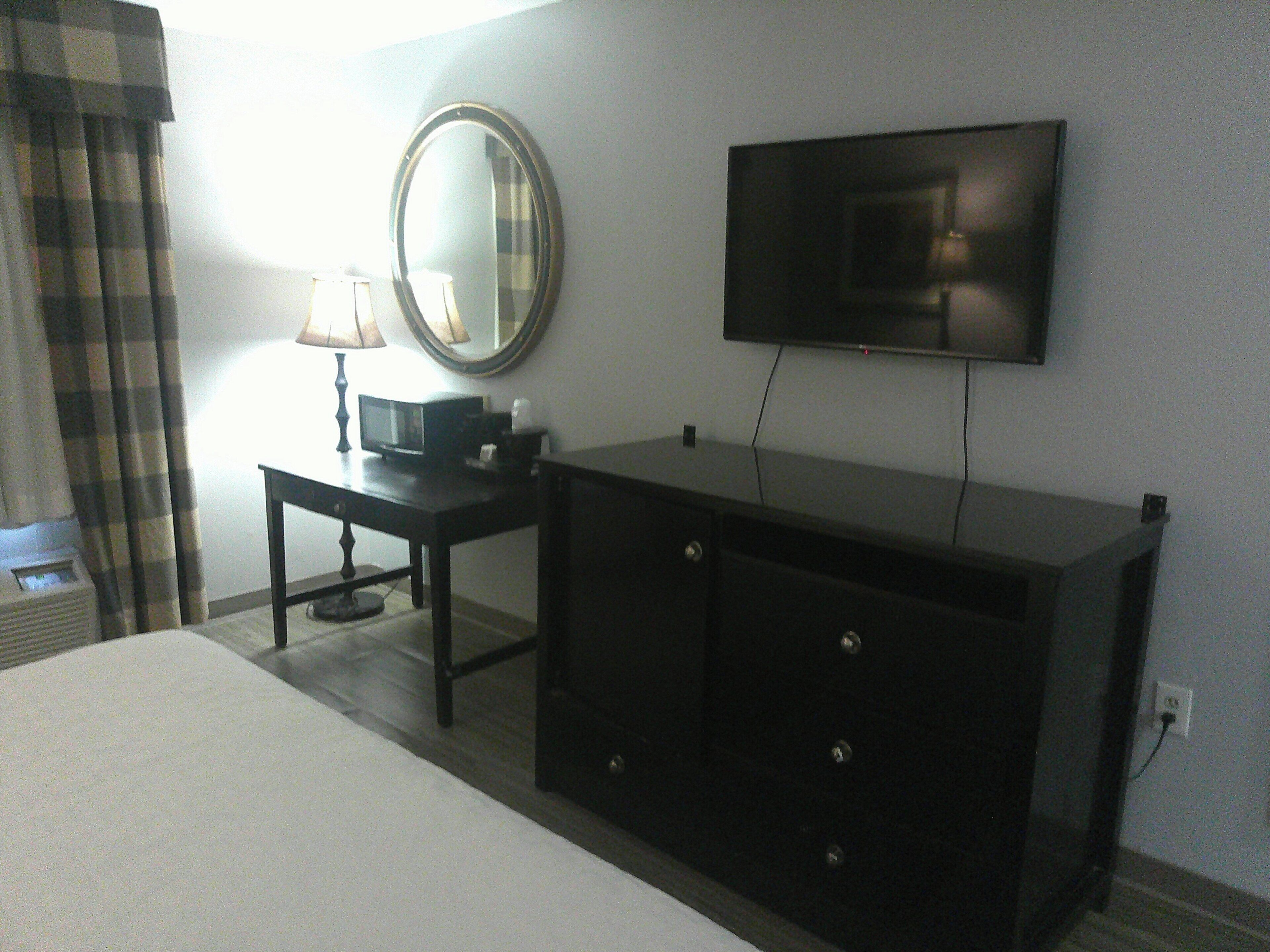 Une chambre d’hôtel avec un lit, une commode, un téléviseur fixé au mur, un miroir et une lampe sur une petite table.
