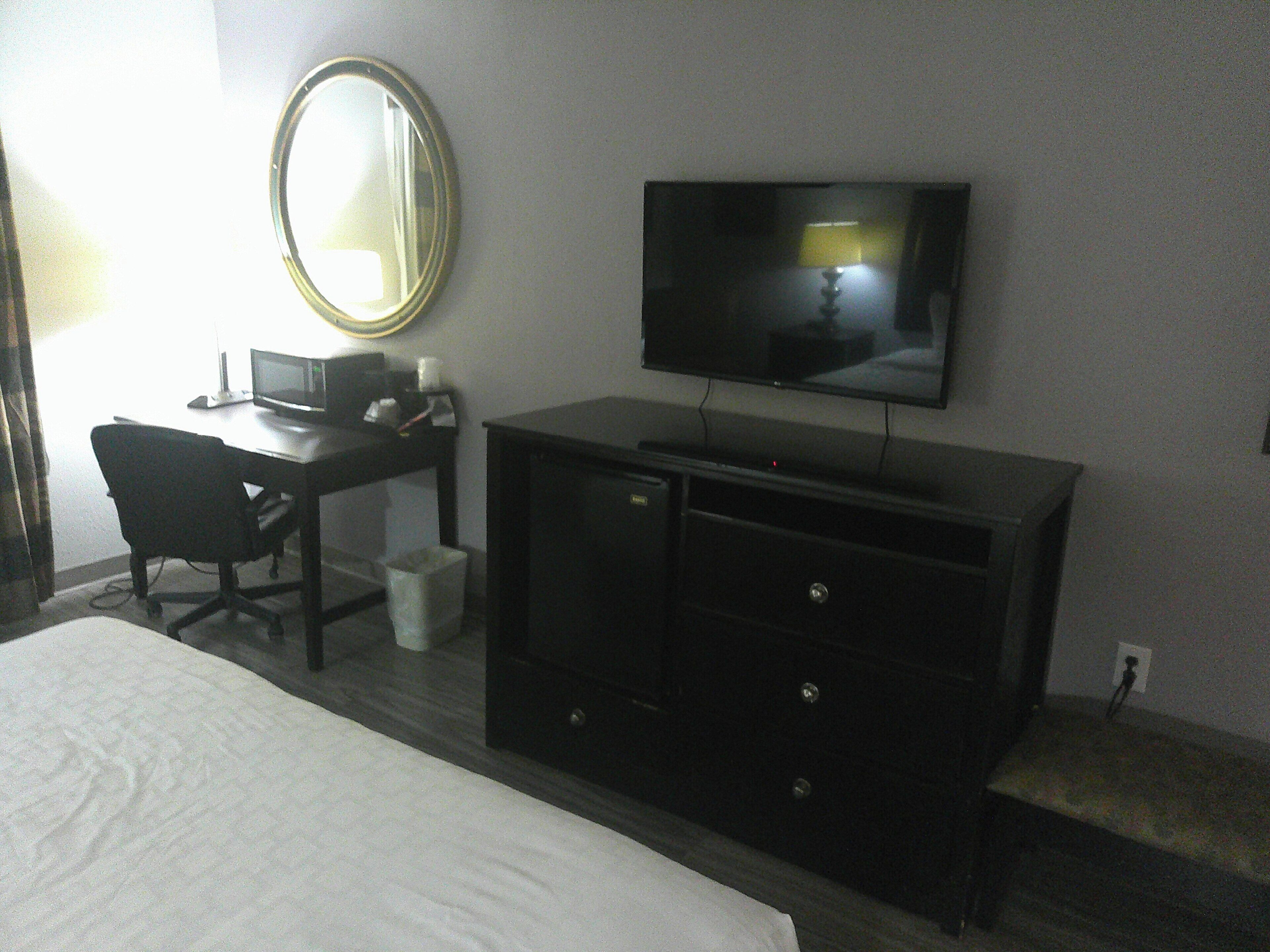 A hotel room with a bed, a desk with a computer, a television, and a mirror.