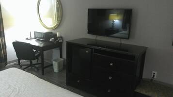 Quarto de hotel com uma cama, uma mesa com computador, televisão e espelho.