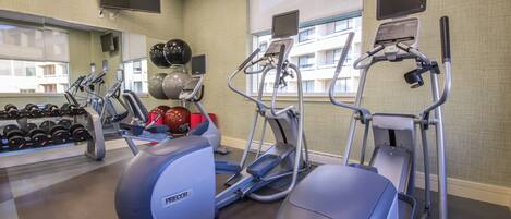 A gym with treadmills, an elliptical, dumbbells, and exercise balls.