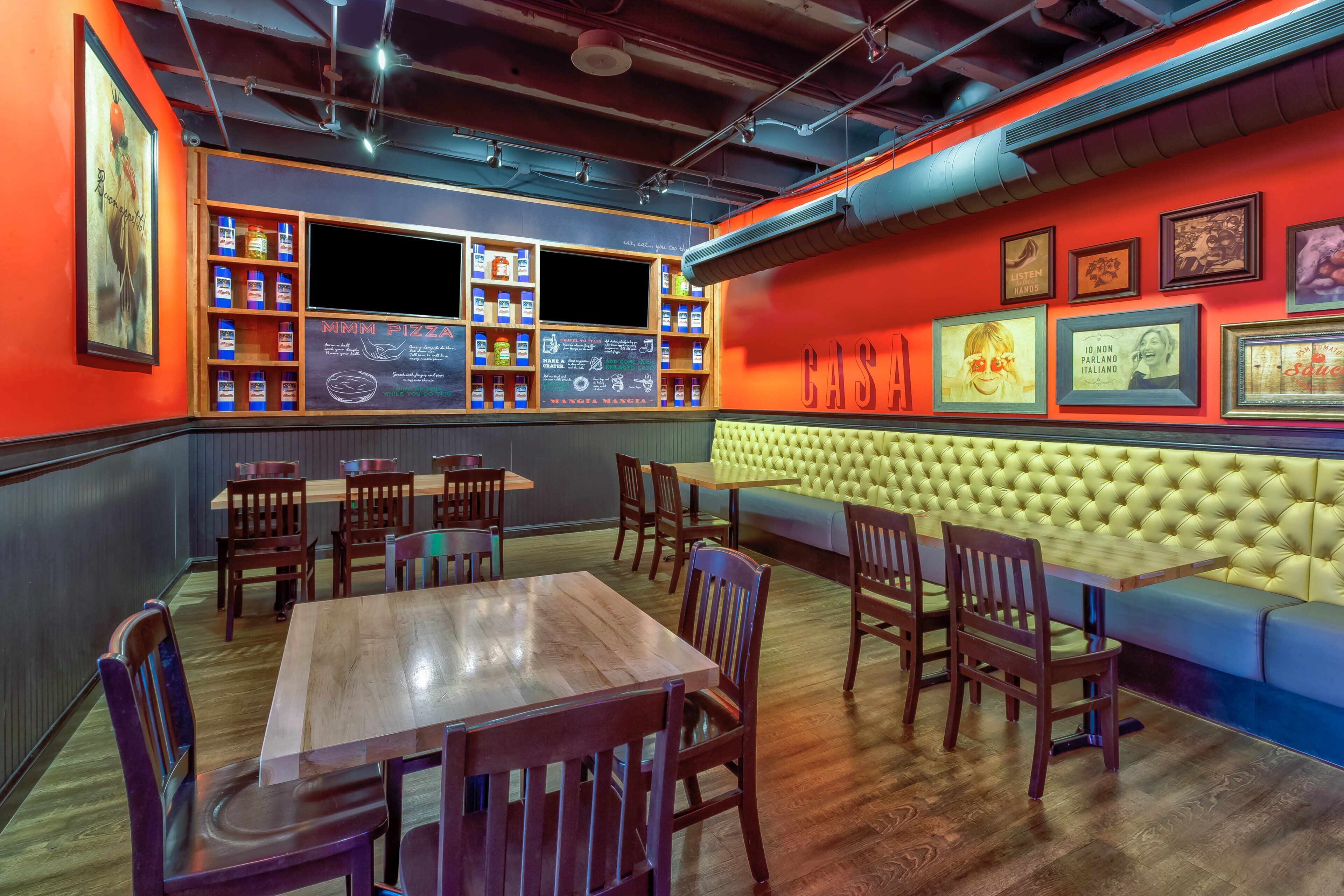 A restaurant interior with wooden tables and chairs, a bar area with shelves of bottles, and a cushioned seating area.