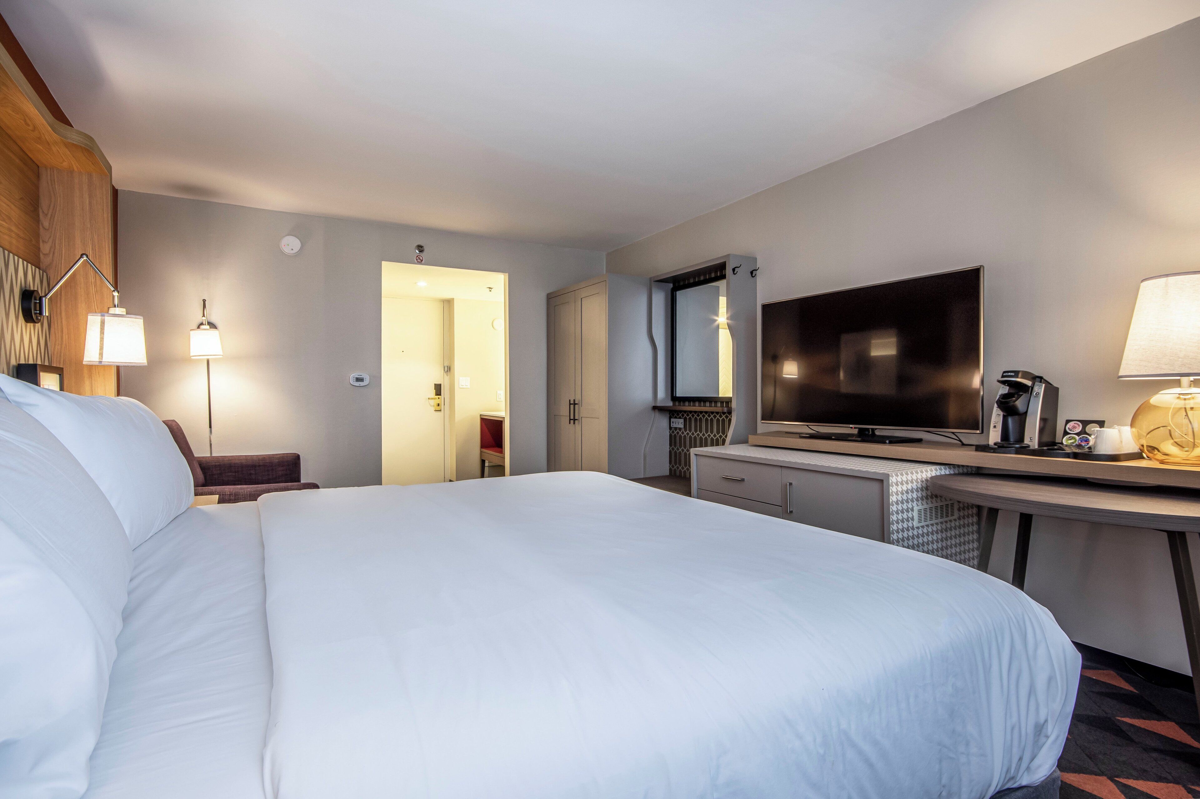 Habitación de hotel con una cama grande, un escritorio, un televisor de pantalla plana, una cafetera y una lámpara.