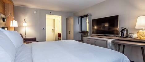 Habitación de hotel con una cama grande, un escritorio, un televisor de pantalla plana, una cafetera y una lámpara.