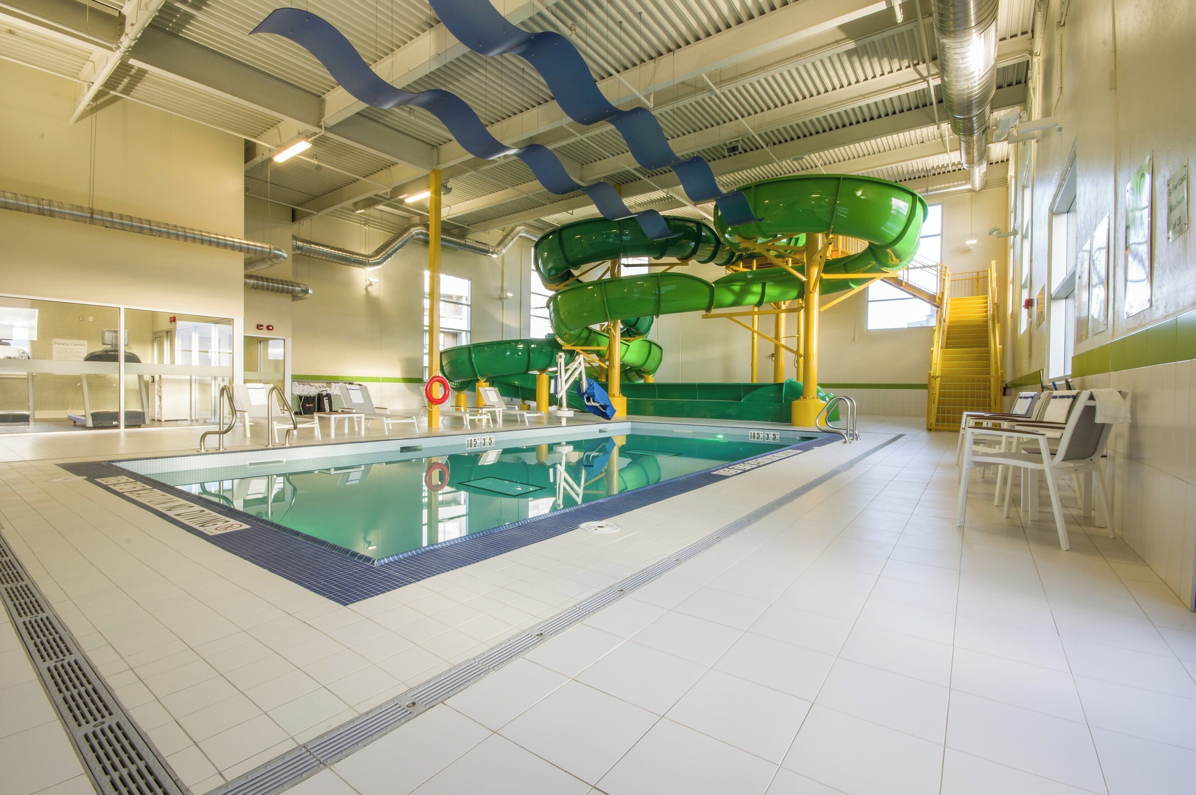 An indoor swimming pool with a water slide, seating areas, and a fitness center.