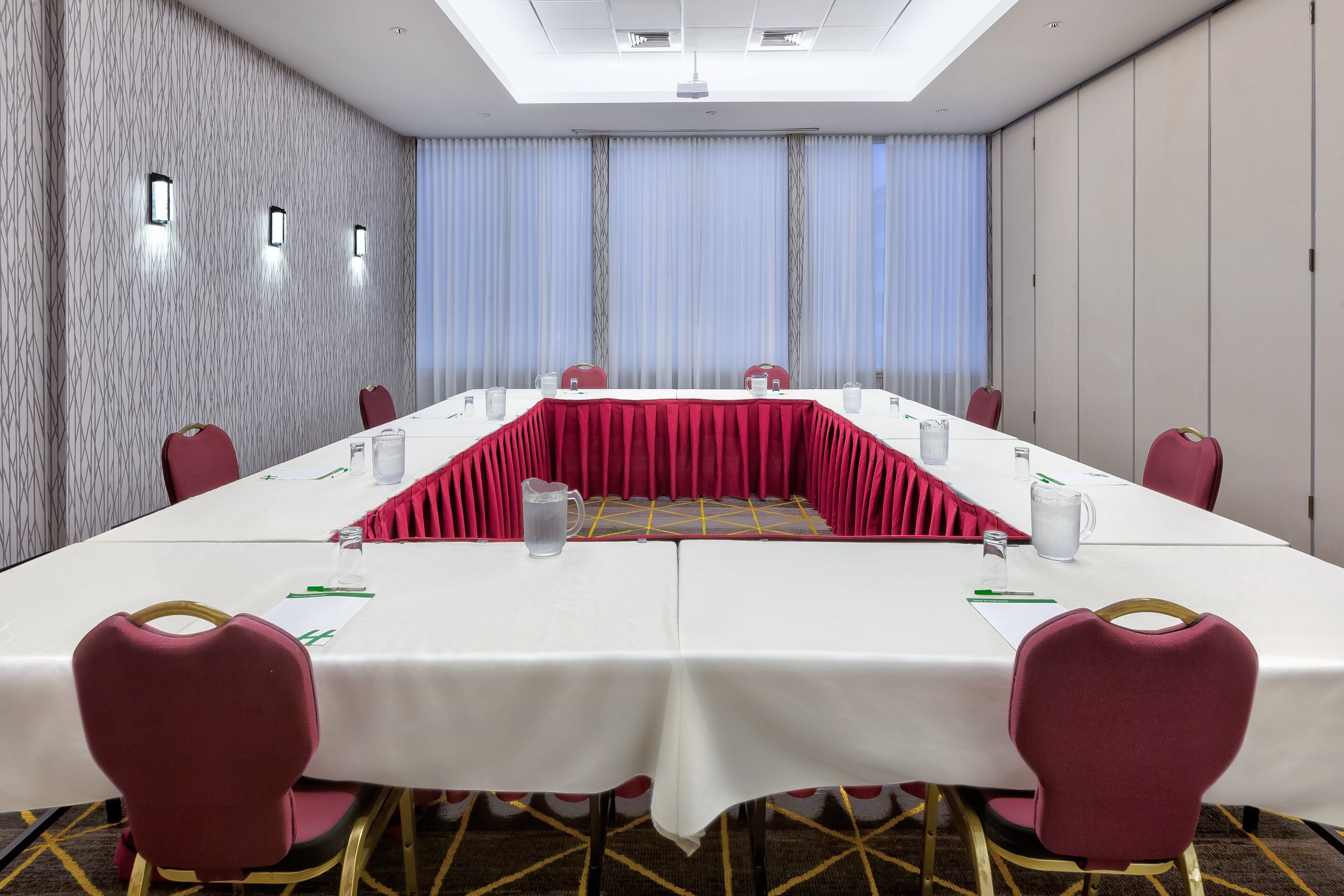 A conference room with a long table, red chairs, and a patterned carpet.
