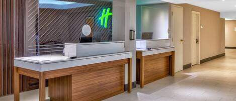 A modern hotel reception area with a wooden reception desk, a glass display case, and a neon sign.