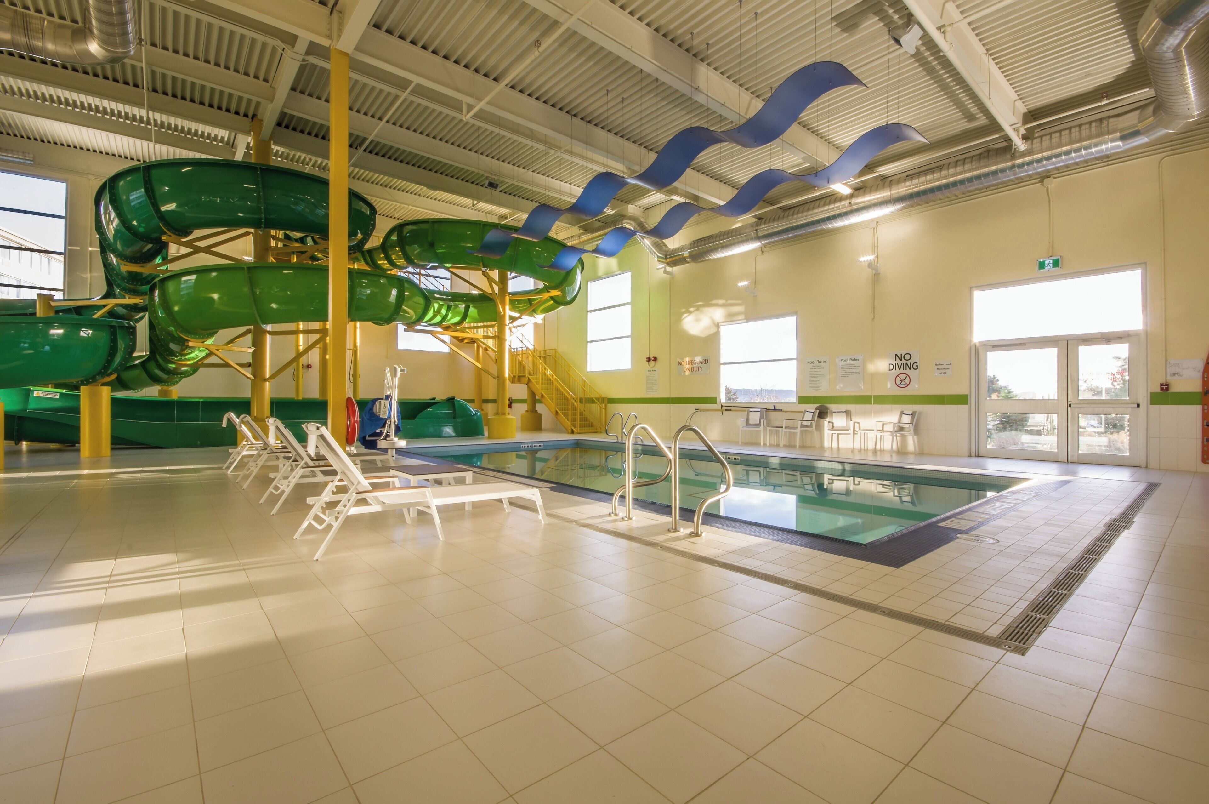 An indoor swimming pool with a water slide, poolside chairs, and a lifeguard station.