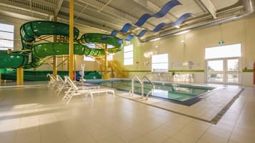 An indoor swimming pool with a water slide, poolside chairs, and a lifeguard station.