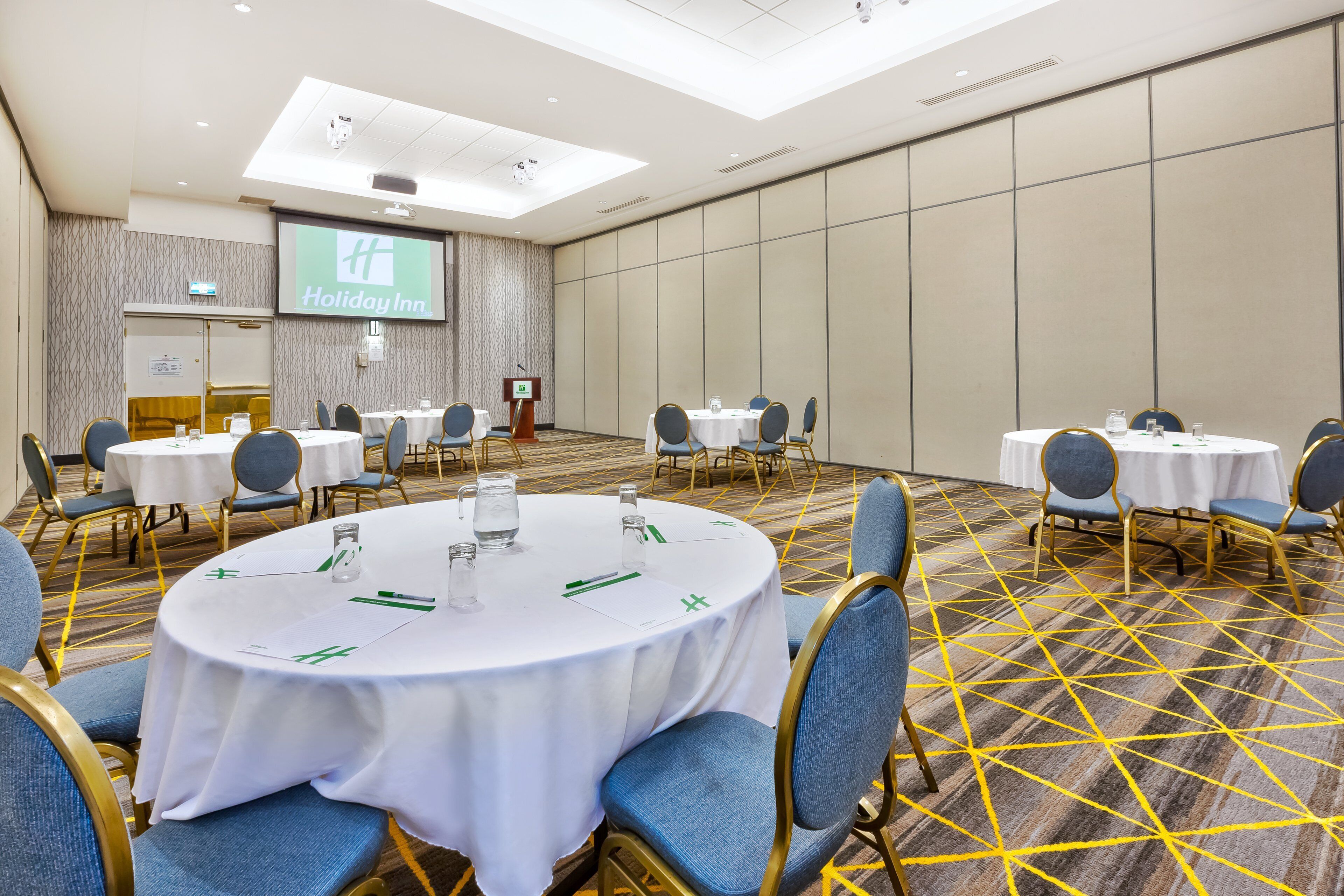 A conference room with round tables, blue chairs, and a carpeted floor.