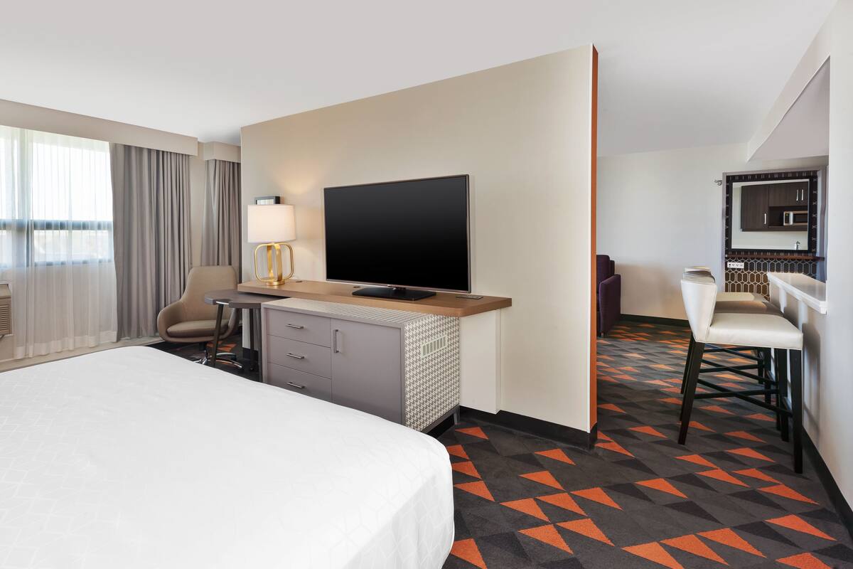 Une chambre d’hôtel équipée d’un lit, d’un bureau, d’une télévision, d’une chaise et d’une salle de bain avec un miroir et un lavabo.